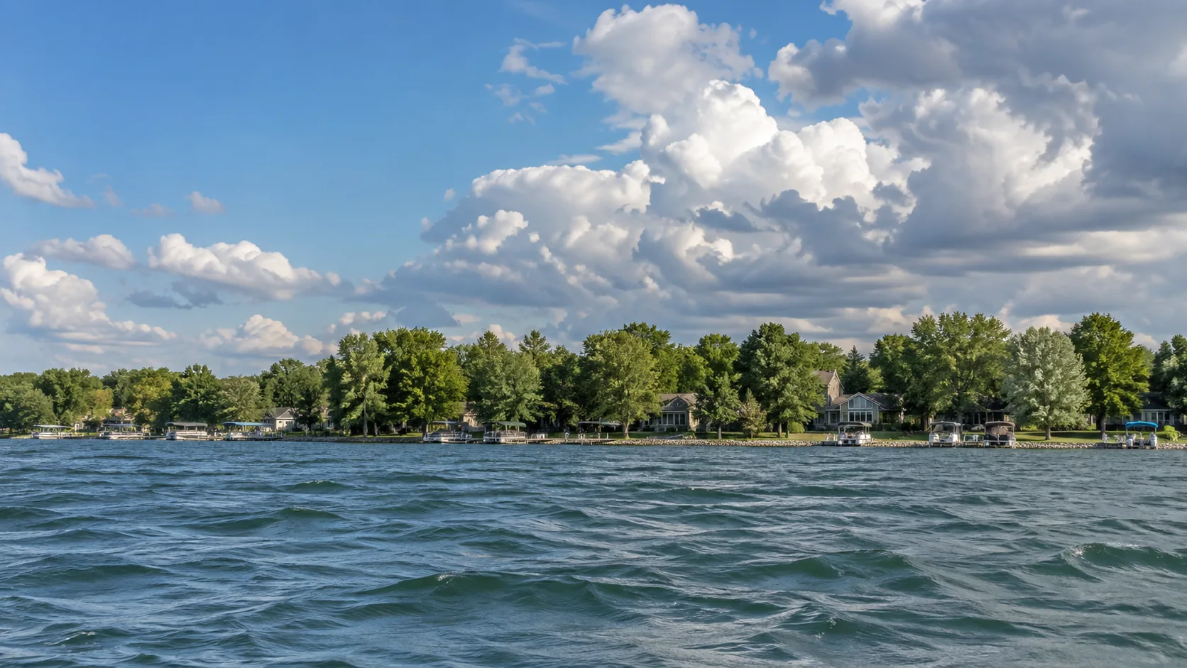The wooded lakefront of Arnolds Park, Iowa seen from the water under broken cloud