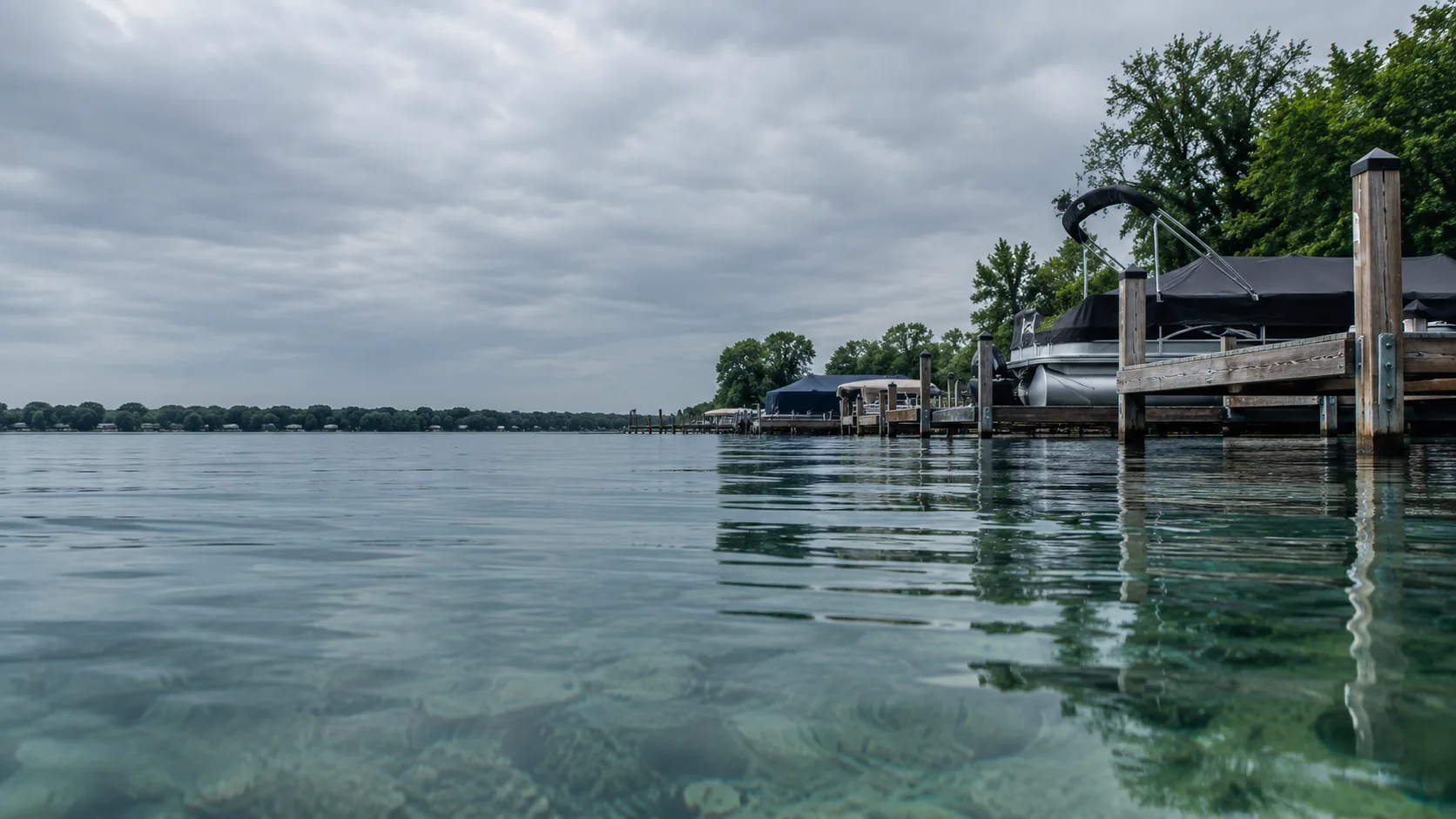 Boat docks along the clear water of West Okoboji Lake, seen from water level under an overcast sky